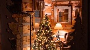 A cozy log cabin interior with a decorated Christmas tree, a fireplace, and a stone wall. - Romantic Private Forrest Hideaway + Heart Shaped Tub + Hot Tub! (Sevierville)