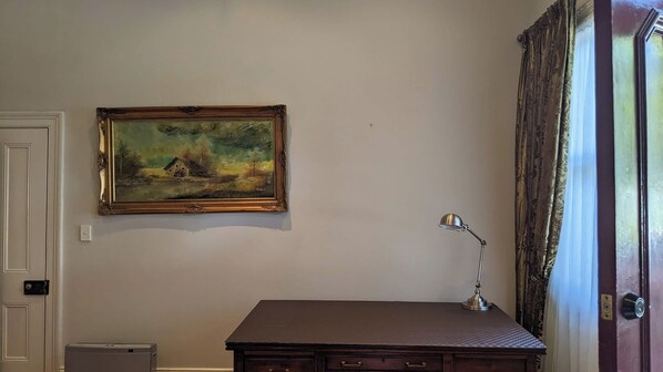 Ein Zimmer mit Schreibtisch, Lampe, einem Bild an der Wand und einer Tür.