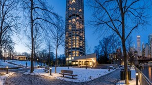 Een hoog gebouw met meerdere balkons, een pad bedekt met sneeuw en een park met bankjes.