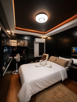 Una habitación de hotel moderna con una cama grande, un ventilador de techo, un equipo de aire acondicionado y un televisor sobre un pedestal.