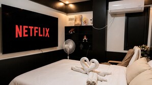 Et moderne hotelværelse med en stor seng, et vægmonteret fjernsyn der viser 'NETFLIX', en loftsvifte og en aircondition.