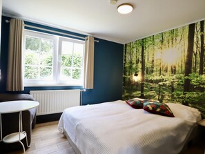 Une chambre avec un lit, une fenêtre, un radiateur et une fresque représentant une forêt sur le mur.