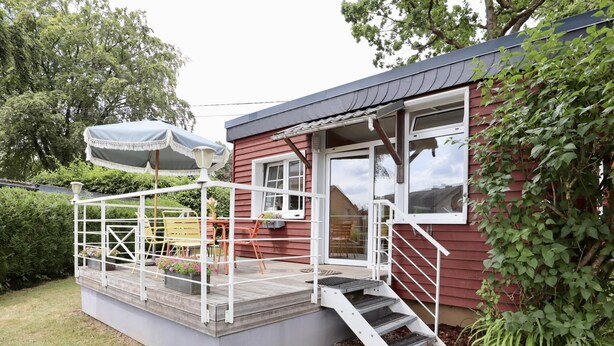 Een klein huis met een veranda, een tafel en stoelen.