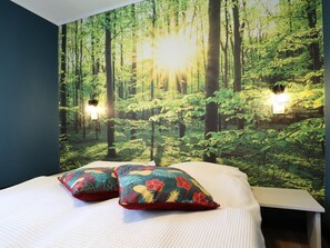 Une chambre avec un décor mural représentant une forêt, deux coussins et deux lampes fixées au mur.