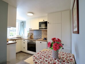 A compact kitchen with white cabinetry, a microwave, a stove, and a sink. There's a table with a floral tablecloth and a vase with flowers. - Charming cottage near Lake Robertville (Robertville)
