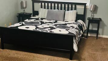Um quarto com cama, duas mesas de cabeceira, janela com persianas e chão coberto por carpete.