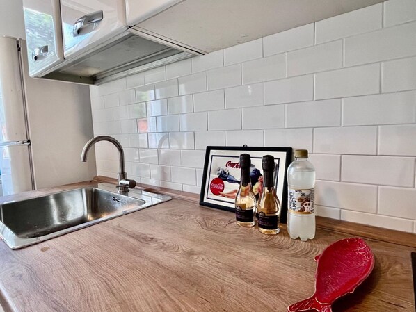 A kitchen with a stainless steel sink, a framed picture, and three bottles of ginger beer on the counter. - Villa Blu di Norsi: 100 steps to sea and peace (Capoliveri)