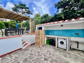 A patio area with a stone floor, outdoor seating, a washing machine, and a tiled backsplash. - Villa Blu di Norsi: 100 steps to sea and peace (Capoliveri)