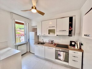 A modern kitchen with white cabinets, a built-in oven, a microwave, and a ceiling fan. - Villa Blu di Norsi: 100 steps to sea and peace (Capoliveri)