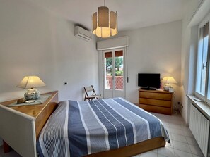 A bedroom with a bed, bedside lamps, a TV, a chair, and a window. - Villa Blu di Norsi: 100 steps to sea and peace (Capoliveri)