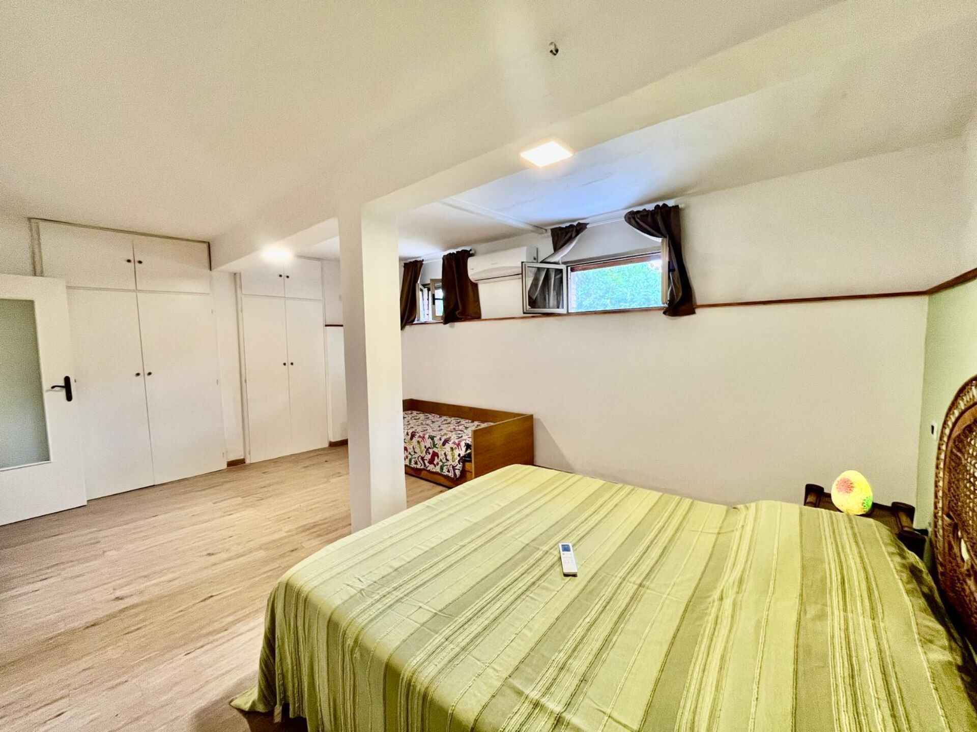 A bedroom with a bed, a wardrobe, a small table, and a window with curtains.