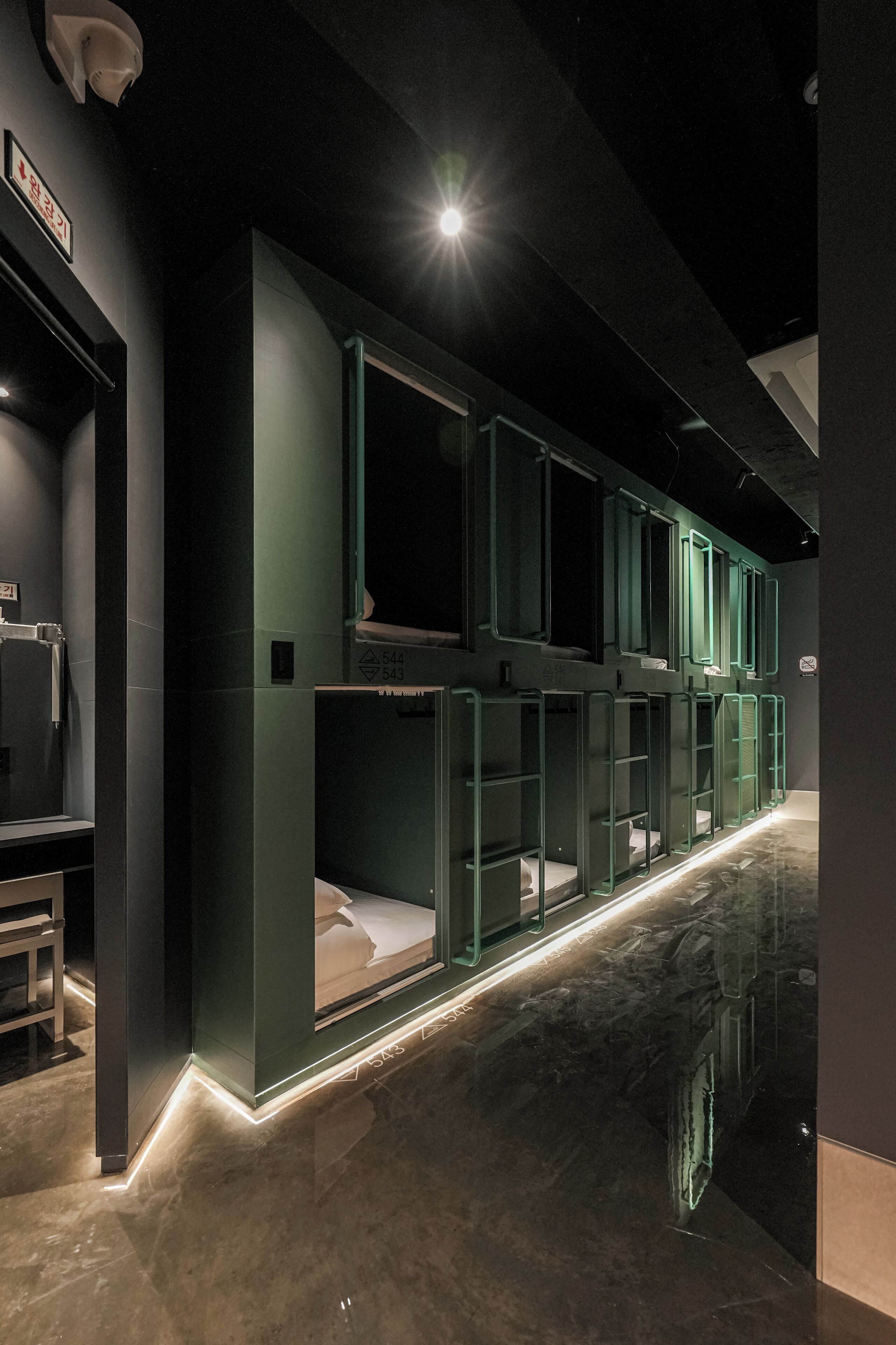 A modern hotel interior with a clean, minimalist design, featuring a central corridor with glass partitions and a polished marble floor.