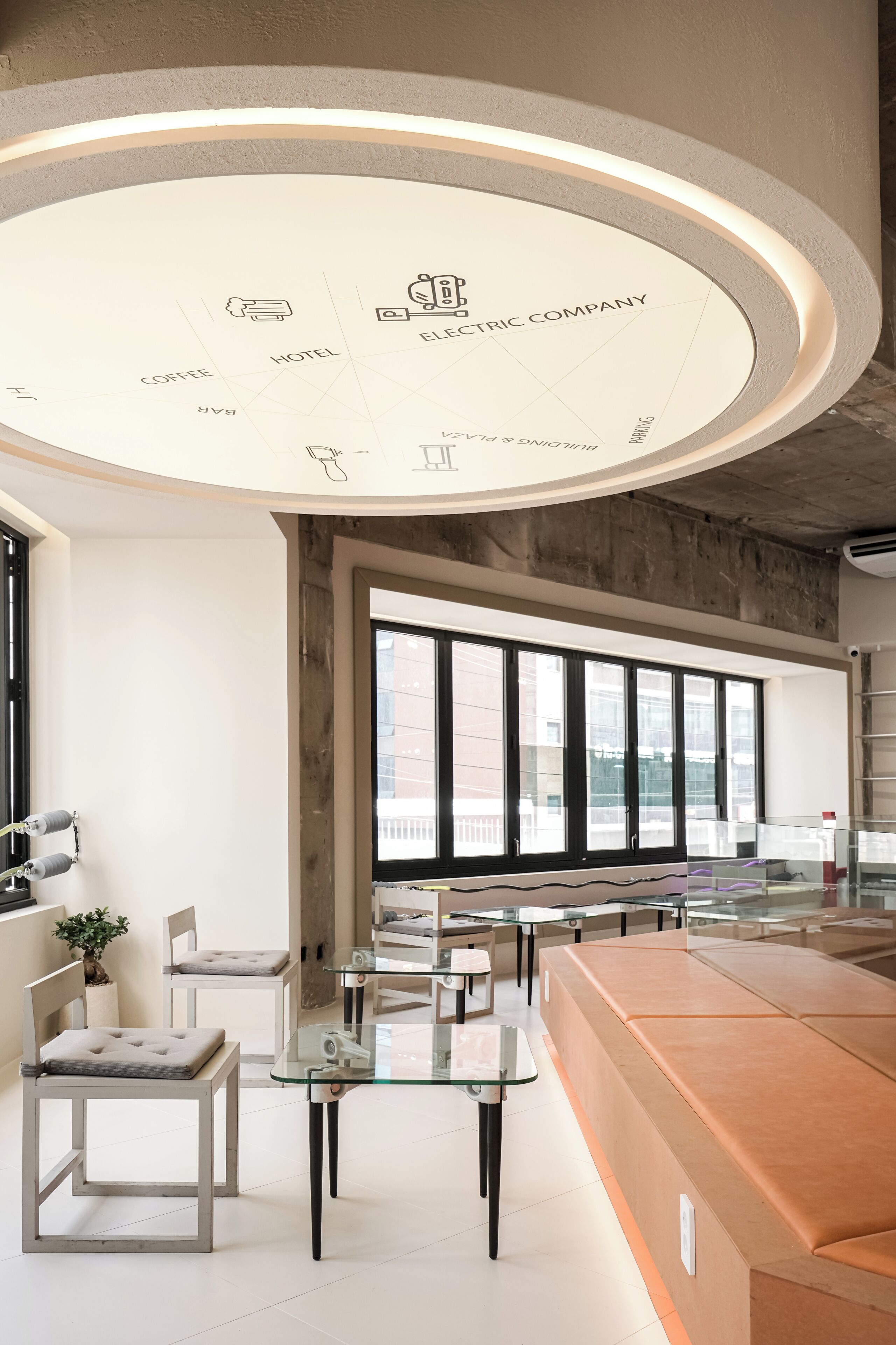 Ein modernes Hotel-Interieur mit einer zentralen, runden Leuchte, Sitzbereichen und großen Fenstern.