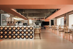 Un bar moderno con una barra larga, diversas opciones de asientos y una amplia selección de botellas y vasos a la vista.