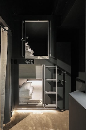 Una cama litera con una pequeña ventana, una mesita de noche y una estantería.