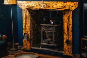 Ein traditioneller Kamin mit hölzernem Sims, ein alter Kochherd und eine dunkelblaue Wand.
