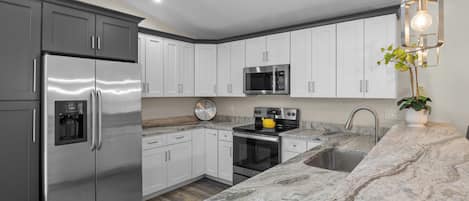 Una cocina moderna con electrodomésticos de acero inoxidable, muebles de cocina blancos, encimera de granito y una lámpara colgante.