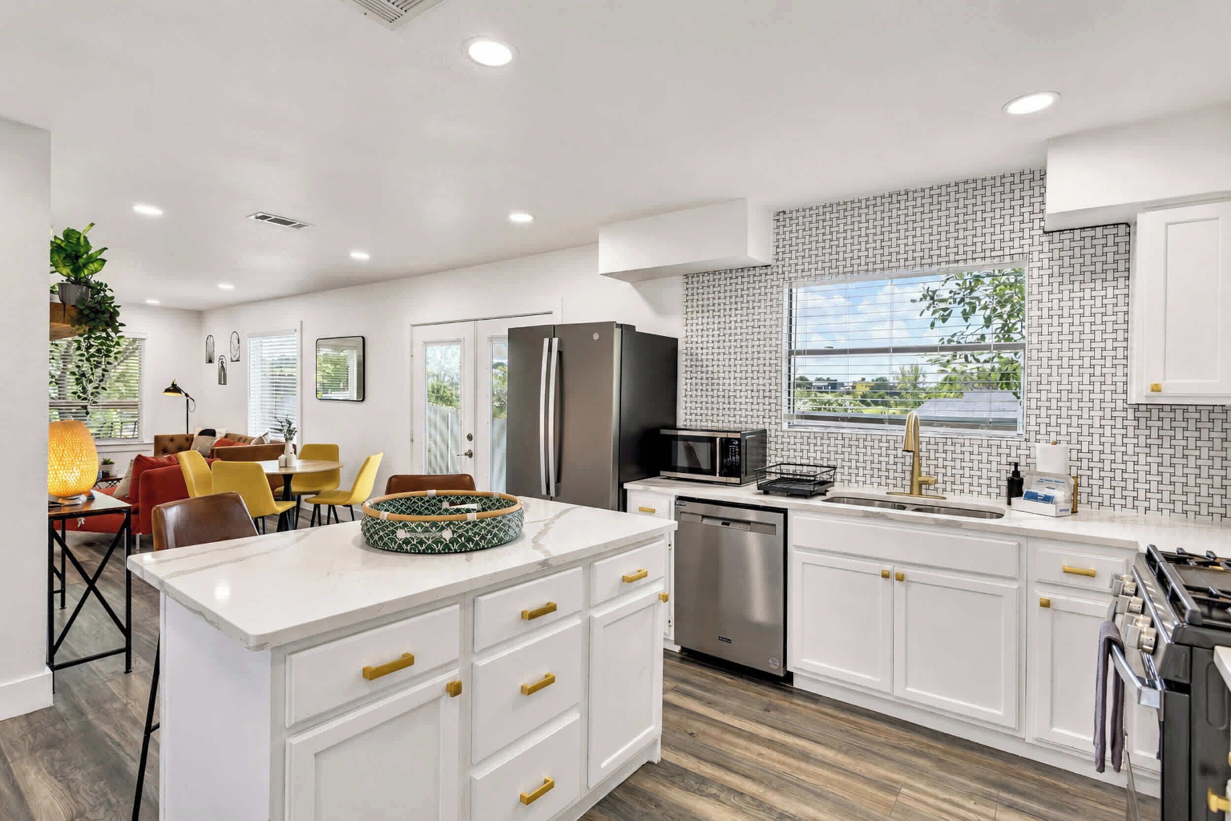 A modern kitchen with white cabinetry, a stainless steel refrigerator, a dishwasher, and a large window with a view.