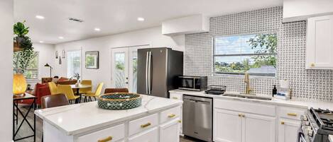 A modern kitchen with white cabinetry, a stainless steel refrigerator, a dishwasher, and a large window with a view.