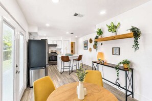 Une cuisine moderne avec des meubles blancs, un réfrigérateur noir et un coin repas avec des chaises jaunes et une table en bois.