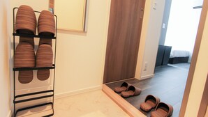 Een gang met een schoenenrek, een spiegel, een houten deur en een bed op de achtergrond.