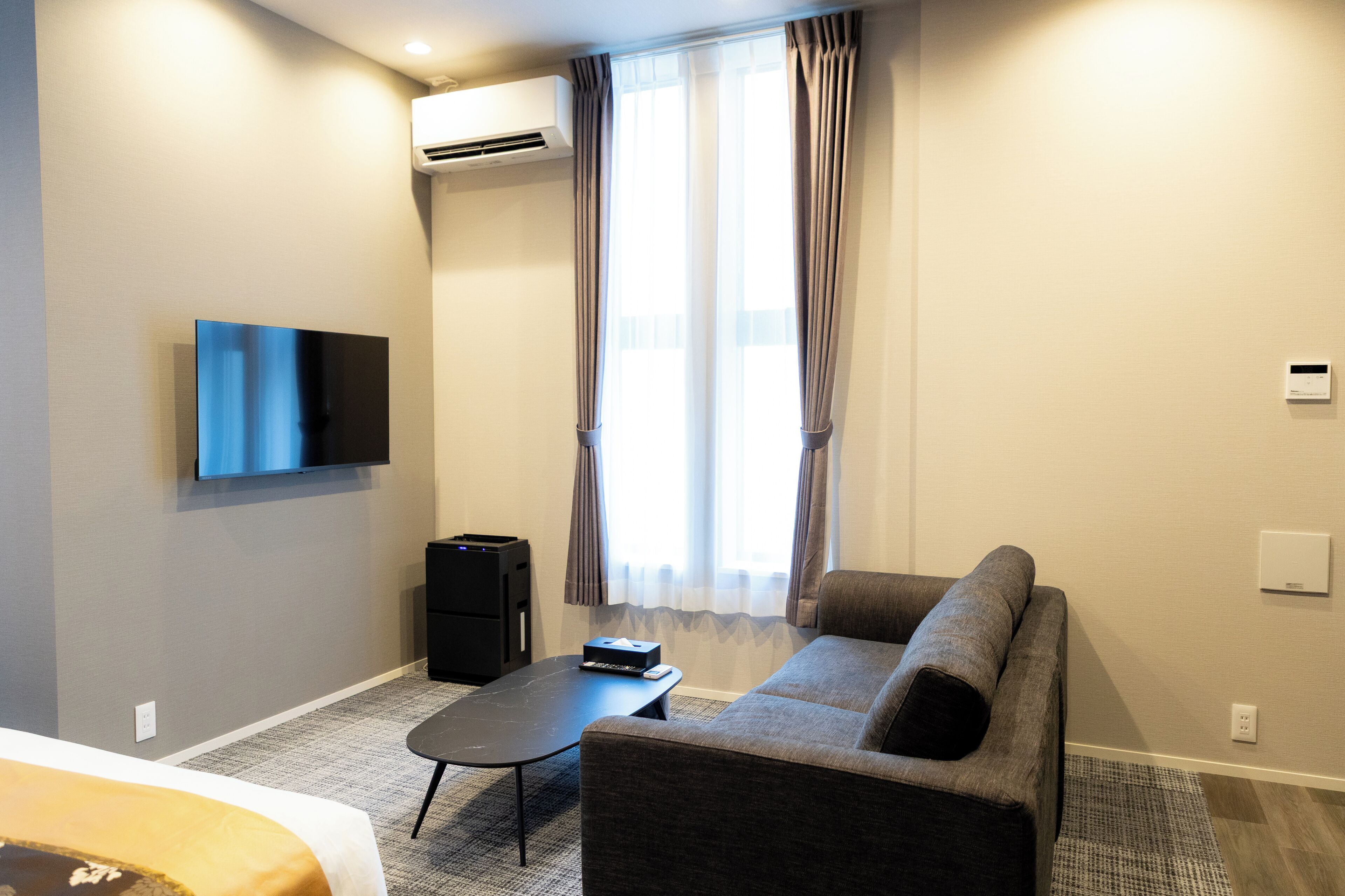 Una camera d'albergo moderna con TV a schermo piatto, un divano, un tavolino, una scrivania e un condizionatore d'aria.