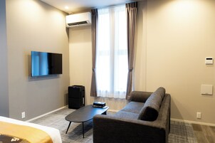 Ein modernes Hotelzimmer mit Flachbildfernseher, einer Sitzecke, einem kleinen Tisch, einem Schreibtisch und einer Klimaanlage.