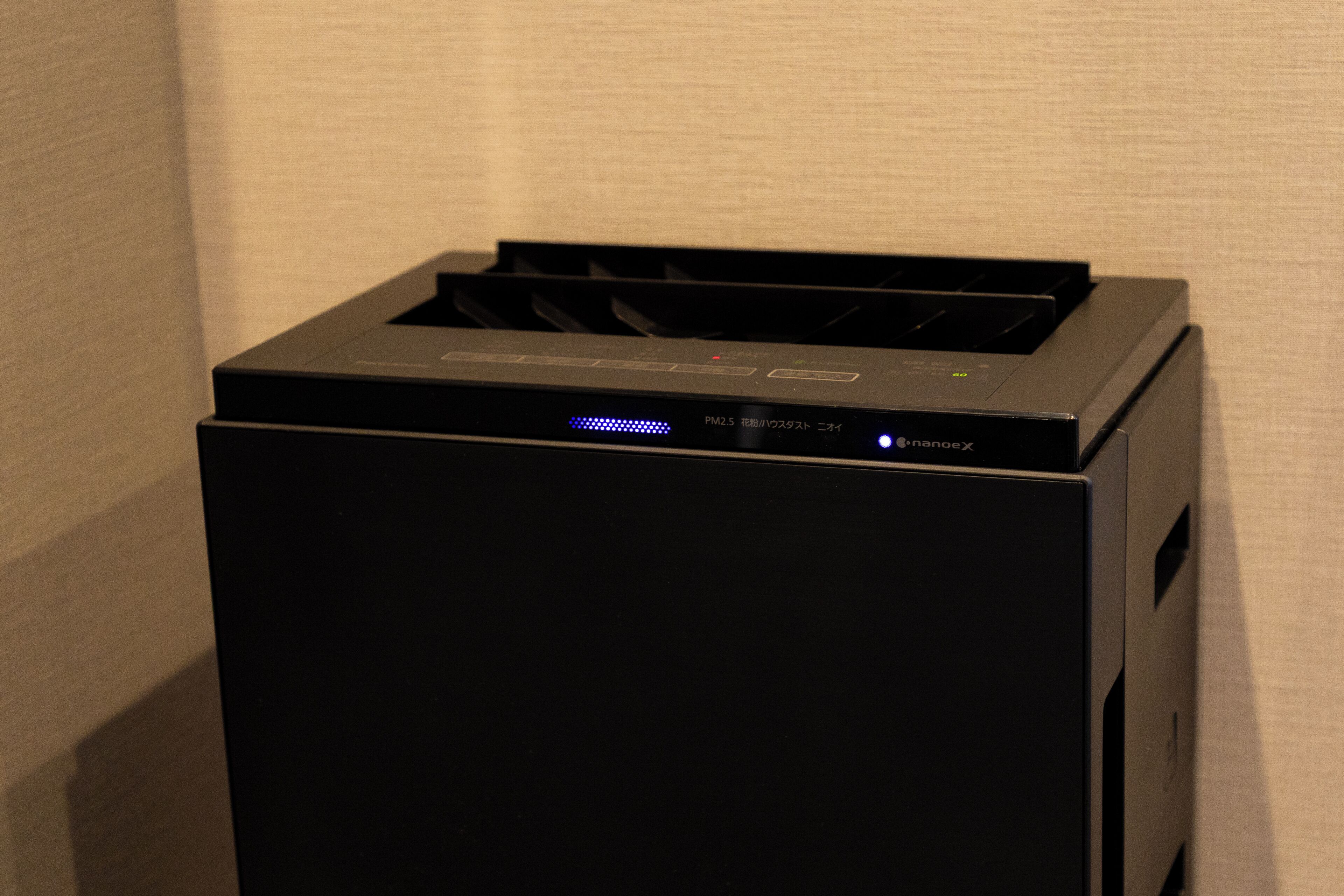 A black printer with a blue light indicator, located against a plain wall.