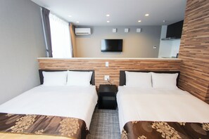 Ein Hotelzimmer mit zwei Betten, einem an der Wand montierten Fernseher und einem kleinen Tisch zwischen den Betten.
