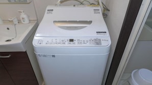 Eine kompakte, weiße Waschmaschine mit Frontlader in einem kleinen Badezimmer, mit Waschbecken und Toilette im Blick.