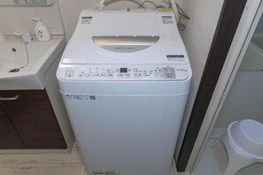 Eine kompakte, weiße Waschmaschine mit Frontlader in einem kleinen Badezimmer, mit Waschbecken und Toilette im Blick.