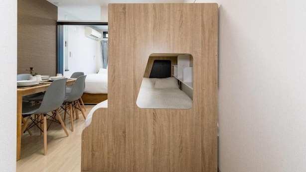 Ein modernes Zimmer mit einer Holzwand, einem Bett, einem Schreibtisch mit Stühlen und einem Fenster.