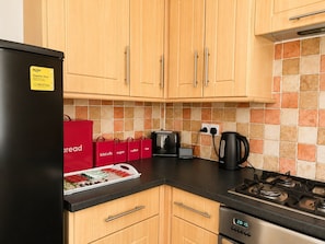 A kitchen with wooden cabinets, a black refrigerator, a stove, a toaster, and a kettle. - Newport Nook by Tŷ SA (Newport)