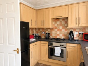 Una cocina compacta con armarios de madera, un refrigerador negro, una estufa y un microondas.
