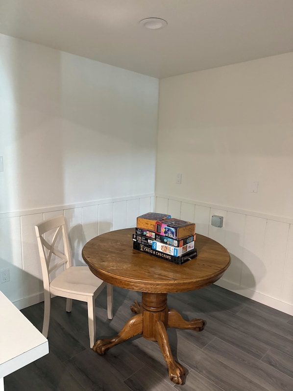 A corner room with a round wooden table, a white chair, and a stack of board games. - Charming 4-bedroom house with AC right on Newman Lake (Newman Lake)