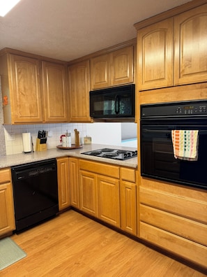 A kitchen with wooden cabinets, a microwave, an oven, and a dishwasher. - Charming 4-bedroom house with AC right on Newman Lake (Newman Lake)