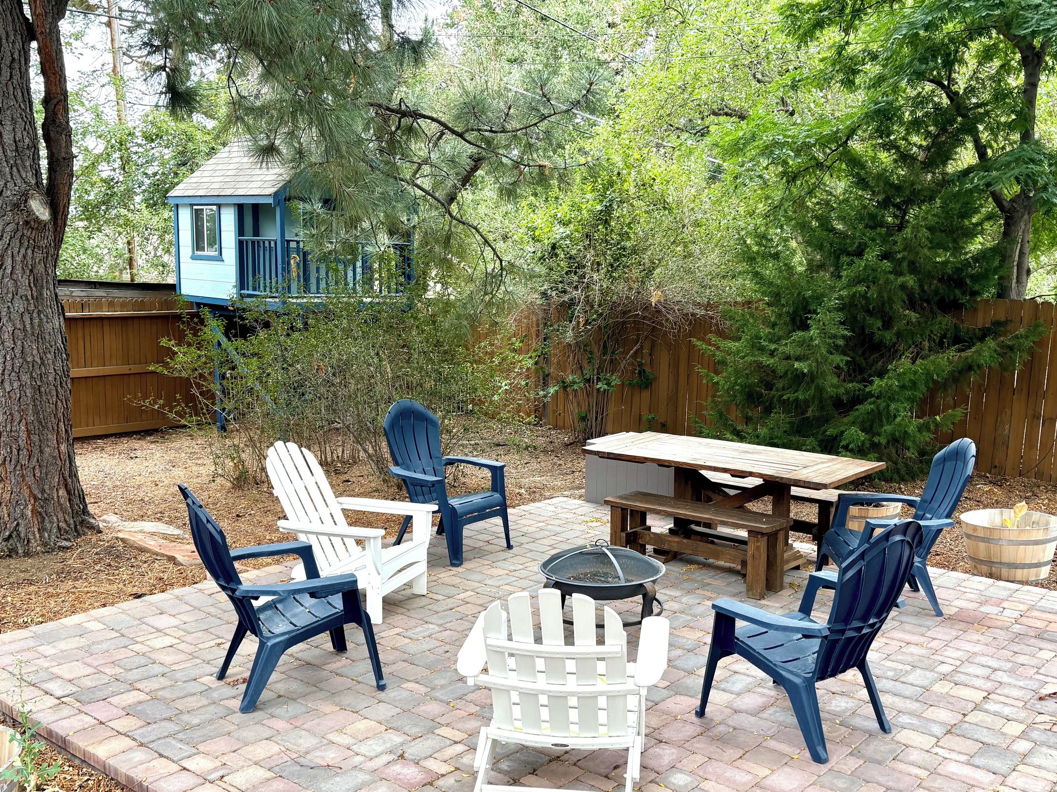 An outdoor patio with Adirondack chairs, a wooden table, and a fire pit.