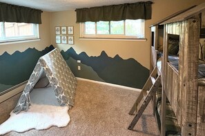 A room with a mountain-themed wall mural, a bed with a wooden headboard, and a window with curtains. - Welcome to Your Family's Ultimate Colorado Basecamp! (Arvada)