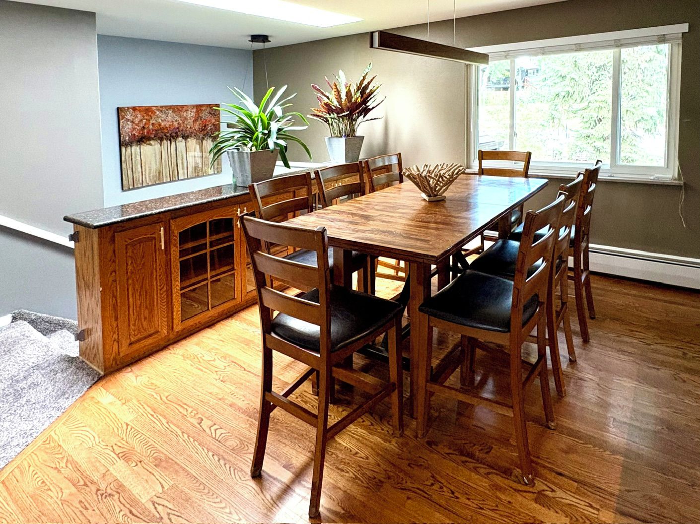 A dining area with a wooden table and chairs, a kitchen counter, and potted plants.