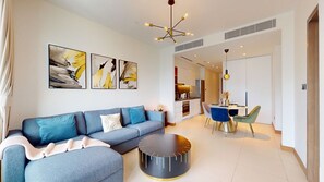 Uma sala de estar moderna com um sofá, uma área de refeições com cadeiras e uma cozinha ao fundo.