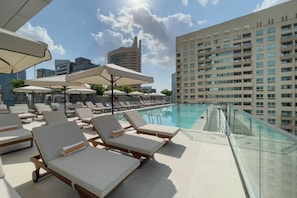 A rooftop pool area with lounge chairs and umbrellas, surrounded by high-rise buildings. - 1 Bed with City and Marina Views l near Mall (Dubai Marina)