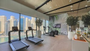 A modern gym with treadmills, stationary bikes, and a large window overlooking a cityscape. - 1 Bed with City and Marina Views l near Mall (Dubai Marina)