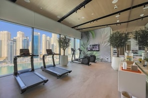 A modern gym with treadmills, stationary bikes, and a large window overlooking a cityscape. - 1 Bed with City and Marina Views l near Mall (Dubai Marina)