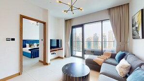 A modern living room with a sofa, a TV, and a balcony with a city view. - 1 Bed with City and Marina Views l near Mall (Dubai Marina)