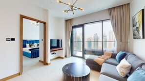A modern living room with a sofa, a TV, and a balcony with a city view. - 1 Bed with City and Marina Views l near Mall (Dubai Marina)