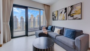 A modern living room with a grey sofa, a round black coffee table, and a city view through large windows. - 1 Bed with City and Marina Views l near Mall (Dubai Marina)