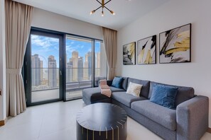 A modern living room with a grey sofa, a round black coffee table, and a city view through large windows. - 1 Bed with City and Marina Views l near Mall (Dubai Marina)