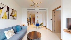 A modern living room with a sofa, a dining area, and a TV. - 1 Bed City and Marina Views l Vida Residences (Dubai Marina)