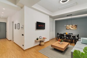 Ein modernes Wohnzimmer mit einem Netflix-Schild, eine Essecke mit Tisch und Stühlen sowie ein graues Sofa.
