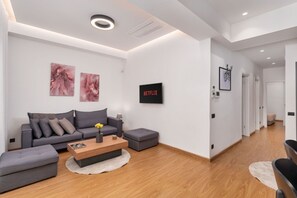 Una sala de estar moderna con un sofá gris, una mesa de centro de madera y un televisor de pantalla plana mostrando 'NETFLIX'.